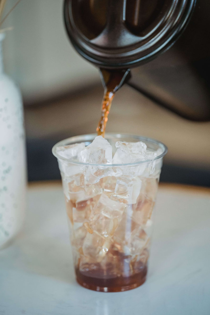 Kalter Kaffee wird aus einer Kanne in einen Becher voller Eiswürfel gegossen