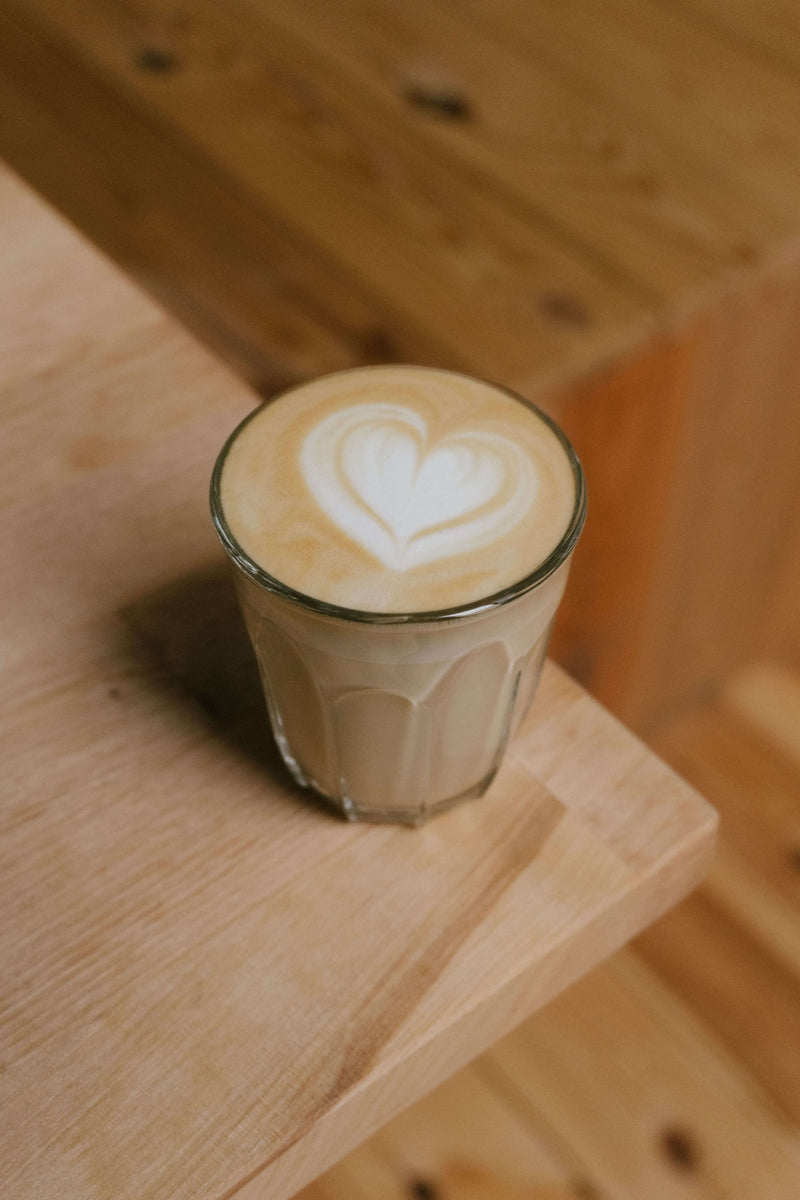 Flat White im Glas mit Herz aus Milchschaum auf einem Holztisch
